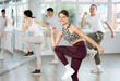 © JackF - Enthusiastic young fit girl in activewear with captivating smile energizing group during dance fitness class in well-lit mirrored studio