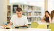 © JackF - Guy reading books at table and writing notes in a notebook in a university library - preparing for exams