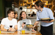 © JackF - Waiter brings an order of food for a couple in a cozy restaurant. Man and woman drinking wine while waiting for food from waiter