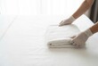 © Stitch - A hotel housekeeper in white gloves neatly folds a fresh white towel on a perfectly made bed.