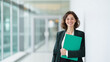 © Favio - Professional businesswoman finance advisor holding green folder in modern bank hallway representing investment management and financial consulting with copy space.