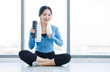 © Bangkok Click Studio - Asian young beautiful happy woman fit sporty healthy in sportswear with towel relax sitting on floor holding water bottle after hard workout exercise training in bright fitness gym wellness lifestyle.
