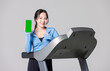 © Bangkok Click Studio - Asian young beautiful cheerful woman sport girl in sportswear exercise holding mobile smartphone with blank green screen showing on treadmill athlete training, gray background studio healthy wellness.