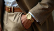 © Maryna - Man wears gold wristwatch and brown suit jacket. Close up shot of person in formal attire showing luxury accessory, wristband, and clothing. Gentleman has elegant style.