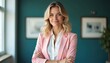 © Maryna - Smiling businesswoman with blonde hair wears pink blazer. Confident woman stands with arms crossed in office. Professional female poses, looking happy and successful in modern workspace.