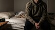 © 24DIY - Man wearing a hoodie sitting alone on a bed in a dark room an alarm clock displays 3 17 AM on the nightstand
