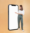 © sitthiphong - Happy Asian business woman pointing at large smartphone mockup with blank screen on beige background.