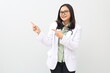 © ArvStd - Smiling Asian adult female doctor standing wearing doctor's coat, stethoscope around neck, pointing with finger sideways at empty space, showing health advertisement, information or news.
