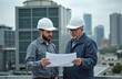 © Maryna - Two engineers in hard hats look at blueprints on a building rooftop. They discuss a project near HVAC cooling towers with city skyline background. Teamwork and planning.