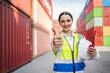 © Wanwajee - Confident female professional with safety vest holding helmet and walkie talkie giving thumbs up in industrial environment. Show success, approval, positive result, reliable workforce.