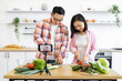 © sofiko14 - An Asian couple is preparing a meal in their kitchen while recording a video for their online audience
