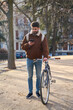 © Oscar - Young man checking smartphone while walking bicycle in urban park