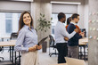 © anatoliycherkas - Businesswoman smiling in modern office, holding tablet, colleagues collaborating and brainstorming with sticky notes