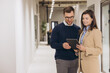 © anatoliycherkas - Businessman and businesswoman walking together in a bright office corridor, using a digital tablet for communication and collaboration