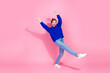 © deagreez - Young woman jumping with joy in blue sweater against pink backdrop for fashion lifestyle and fitness ads