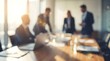 © CuteBee - A soft focus image captures a dynamic business meeting in a modern office, with indistinct figures of professionals collaborating around a large wooden table bathed in sunlight.