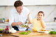 © caftor - Little daughter eats chips in the kitchen, father offers her healthy vegetable salad
