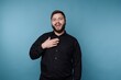 © bodnarphoto - Man stands in front of blue background laughing and posing in black shirt with hand on chest and joyful expression
