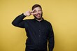 © bodnarphoto - Young man makes silly face and shows peace sign against bright yellow background in indoor setting