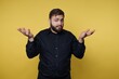 © bodnarphoto - Person in black shirt expressing uncertainty with hands raised in front of yellow background