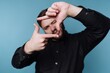 © bodnarphoto - Man makes a frame shape with his hands in front of a blue wall while smiling and posing for the camera during daytime