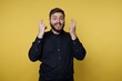 © bodnarphoto - Man shows fingers crossed gesture with a big smile against a yellow background in a studio setting during daytime