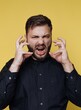 © bodnarphoto - Man expresses frustration with a loud yell against a bright yellow background during an indoor setting