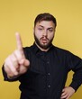 © bodnarphoto - Man standing in front of a yellow background with his hand raised while looking directly at the camera during a casual moment