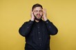 © bodnarphoto - Man holds his head with both hands while making a face against a yellow background with bright lighting in a studio setting