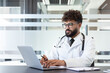 © Liubomir - Young male doctor working on a laptop, providing online consultations and managing patient records in a contemporary medical office, symbolizing digital healthcare and professional assistance