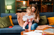 © Maria Vitkovska - Mother and daughter reading paper document together while relaxing on sofa at home
