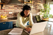 © Davor - Focused woman paying bills on laptop in home kitchen