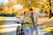 © BGStock72 - Joyful autumn stroll with a bicycle and cups in the park featuring a Korean woman and Caucasian man