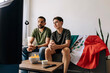 © kleberpicui - Mexican father and teenage son watching a football match quietly at home. Family supporters sitting together on the sofa with national flag, snacks and drinks in the living room.