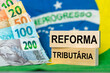 © Rochu_2008 - Tax reform, words written in Brazilian Portuguese on wooden blocks against the backdrop of the Brazilian flag and money. Financial Concept, Taxes in Brazil