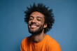 © Serhii - Cheerful portrait of a man with Afro hair wearing an orange T-shirt, winking and smiling in a controlled studio setting