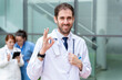 © StockMe - Doctor making ok gesture with medical team in background offering positive healthcare and success
