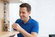 © Stitch - A smiling man in a blue polo shirt installs or adjusts a white Wi-Fi router on a wooden shelf, setting up a home internet network.
