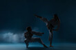 © New Africa - Man and woman in uniforms practicing karate on dark light blue background with smoke