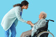 © Pixel-Shot - Young African-American female medical worker with elderly woman on wheelchair against blue background