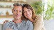 © evgenia_lo - A middle-aged Latino man sits on a sofa while a young Latina woman hugs him from behind, both smiling warmly in their bright living space
