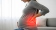© designhunt - Lower back pain during third trimester. Maternal health and spinal pressure issues. Pregnant woman sitting on a sofa and holding her painful lumbar area
