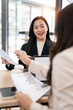 © NAMPIX - Professional Asian women reviewing charts and business documents during a meeting in a bright office.