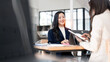 © NAMPIX - Two successful Asian businesswomen collaborating and discussing reports in a bright, modern office workspace.