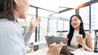© NAMPIX - Happy Asian businesswoman holding a coffee cup while discussing projects with a colleague in a modern office.