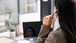 © NAMPIX - Rear view of a professional Asian customer service agent wearing a headset and working at a desk in a modern office.