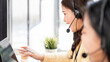 © NAMPIX - Happy Asian customer service agent wearing a headset and smiling while working with a colleague in a modern office.