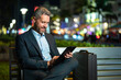 © Volodymyr - Businessman working on tablet outdoors. Businessman with tablet outdoor. Businessman with a tablet on night street. Businessman using tablet, sit on bench. Night business.