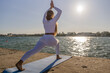 © svetograph - Yoga Woman Water Sunset - Woman in white clothing practices yoga pose on a mat by the water during sunset.