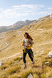© maxbelchenko - A happy hiker with a yellow backpack enjoys the mountain scenery on a hiking trail. The young woman feels the freedom of the outdoors. Concept of hiking, freedom, and adventure.